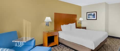 A hotel room with a bed, a blue armchair, a small table, and a nightstand with lamps.