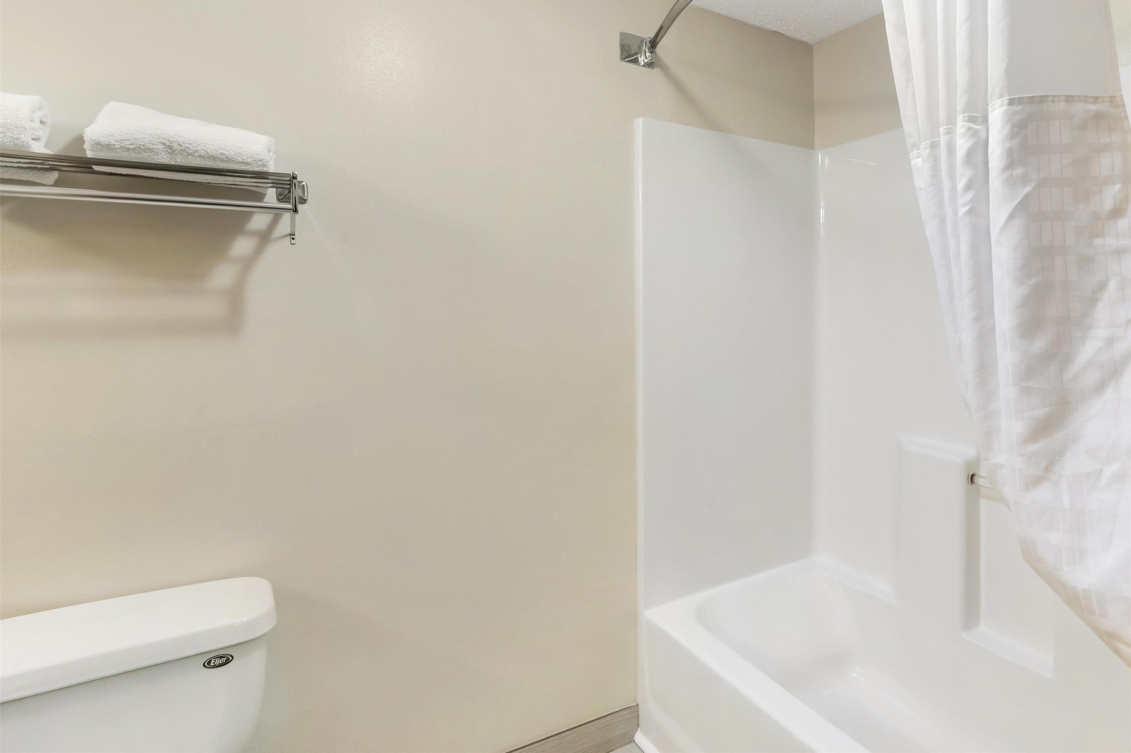 A bathroom with a toilet, a shower with a curtain, and a towel rack with two towels.