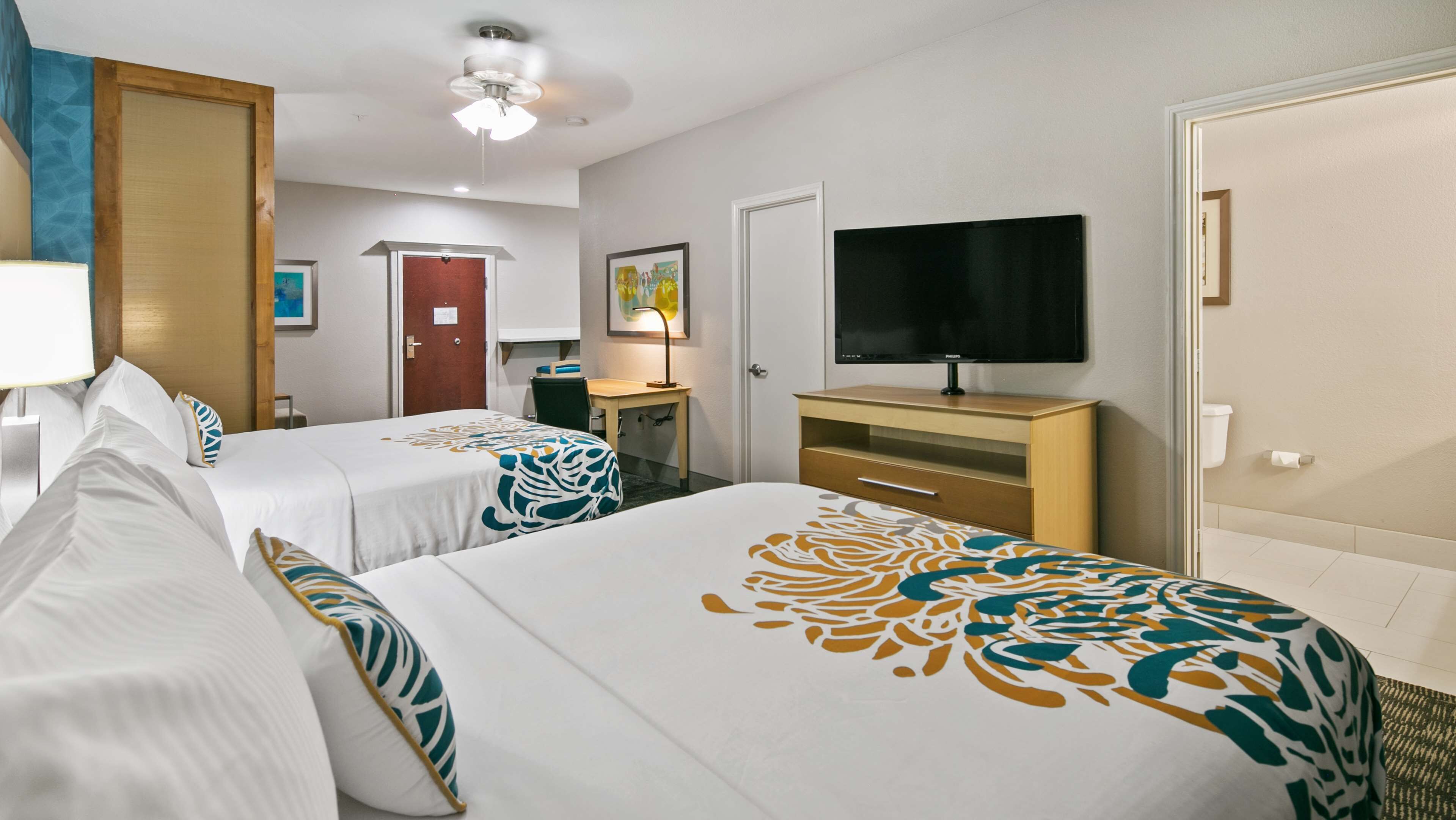 A hotel room with two beds, a desk, a chair, a television, and a door.