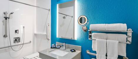 A modern bathroom with a blue accent wall, a white sink, a mirror, a towel rack, and a shower with grab bars.