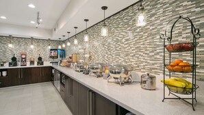 A modern kitchen with a long counter, coffee machines, and a fruit display. - Best Western Plus Houston Atascocita Inn & Suites (Humble)