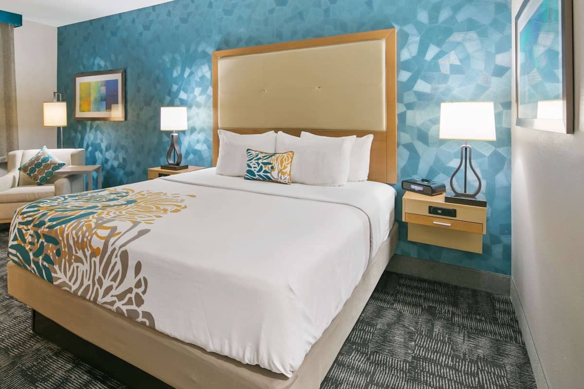A hotel room with a large bed, a chair, a desk, and a nightstand.