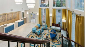 A hotel lobby with a reception desk, seating area with sofas and chairs, a staircase, and large windows with curtains. - Best Western Plus Houston Atascocita Inn & Suites (Humble)