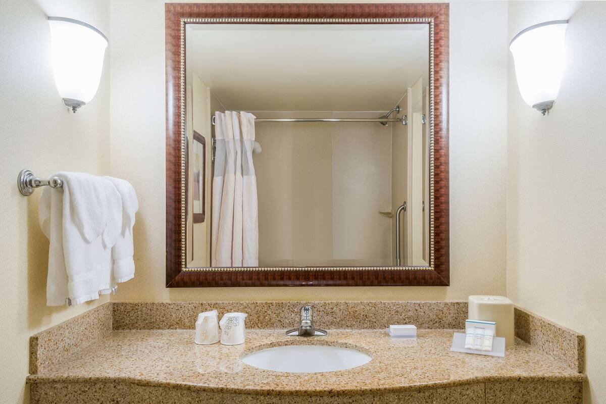 A bathroom with a granite countertop, a white sink, a large mirror, and a towel rack with towels.