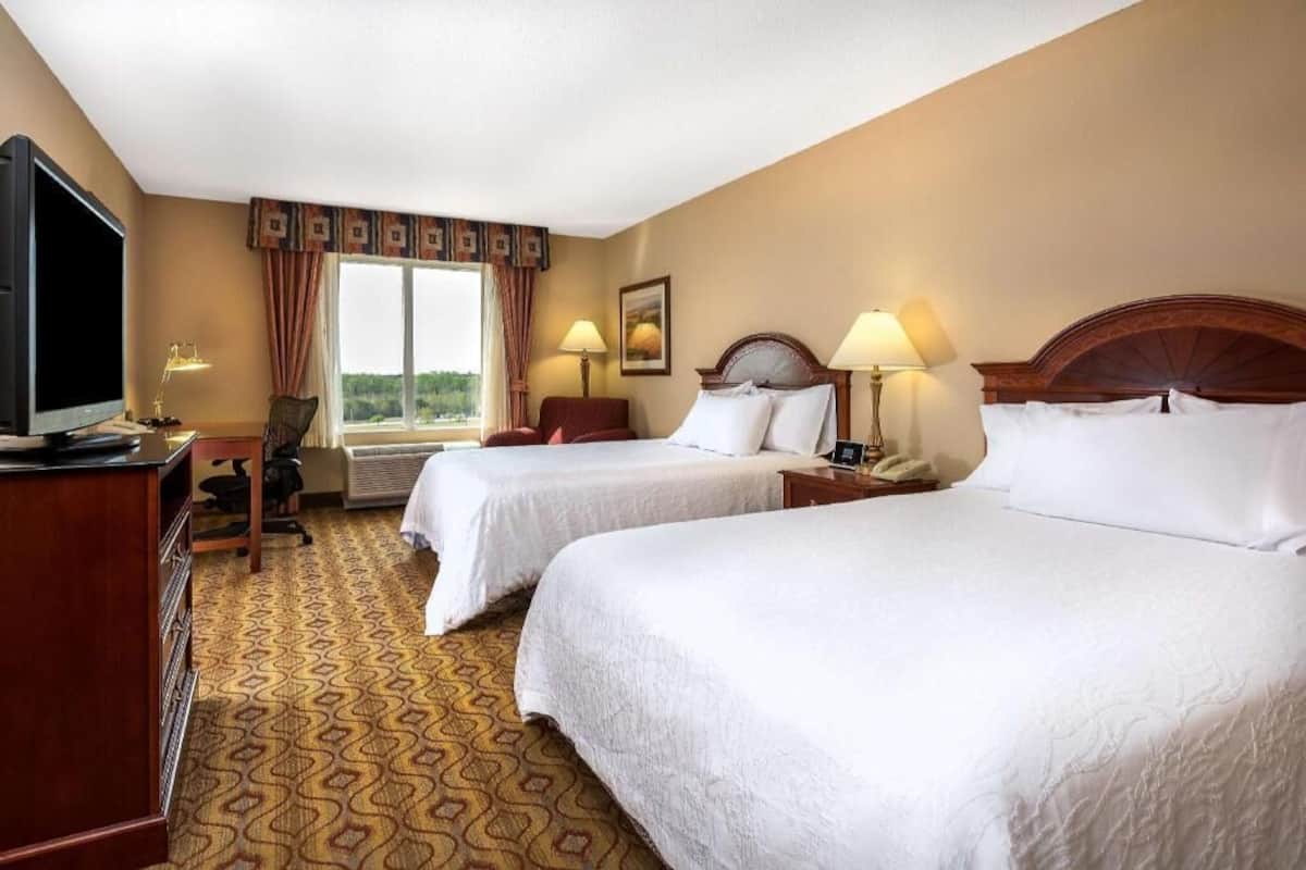 A hotel room with two beds, a television, a desk, and a window with curtains.