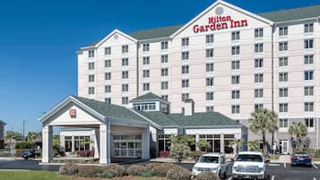 Un hotel Hilton Garden Inn con una entrada central, varios espacios de estacionamiento y un césped bien cuidado.