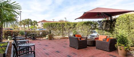 An outdoor patio with brick flooring, outdoor furniture, and a large umbrella providing shade.
