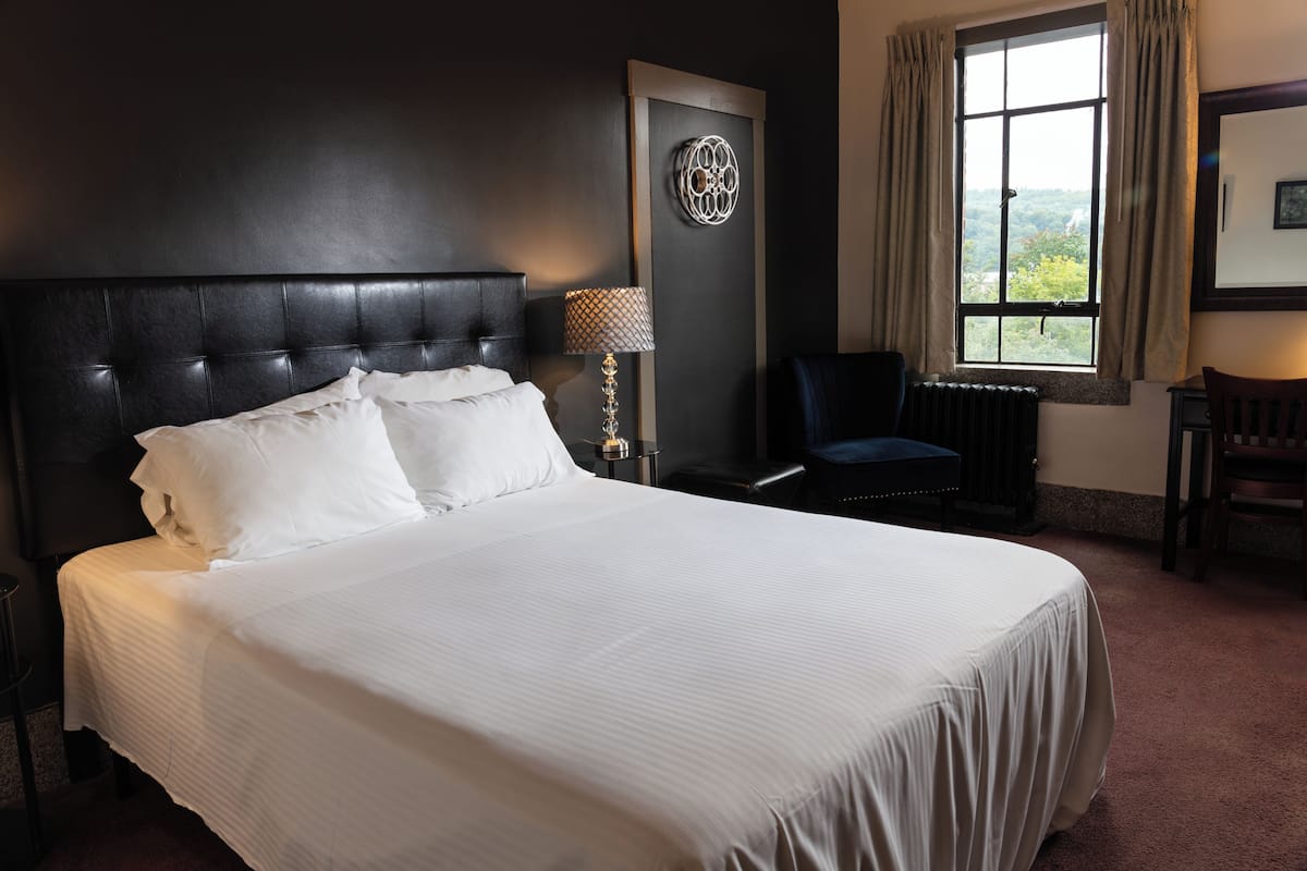 A neatly made bed with white linens, a dark headboard, and a wall-mounted decorative piece.
