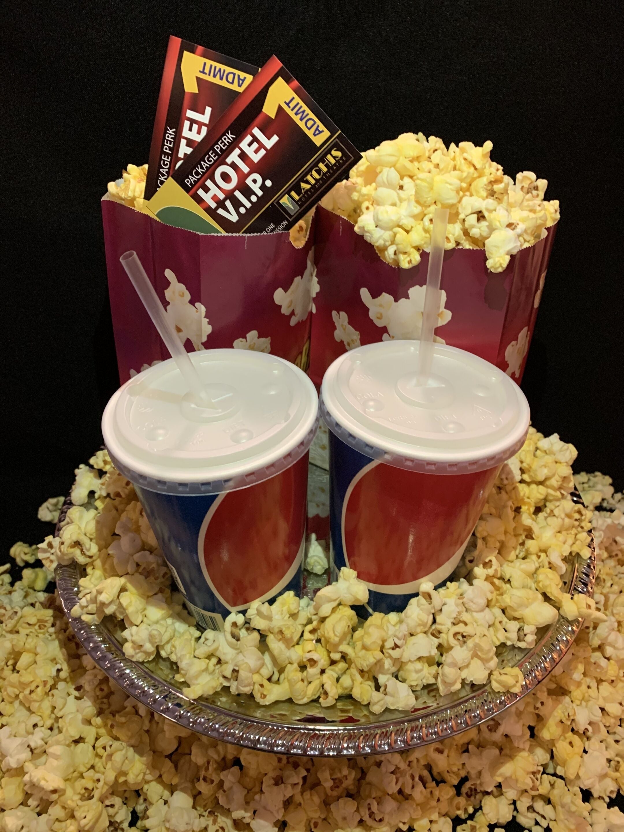 Two popcorn containers with a lid and a straw, placed on a tray filled with popcorn.
