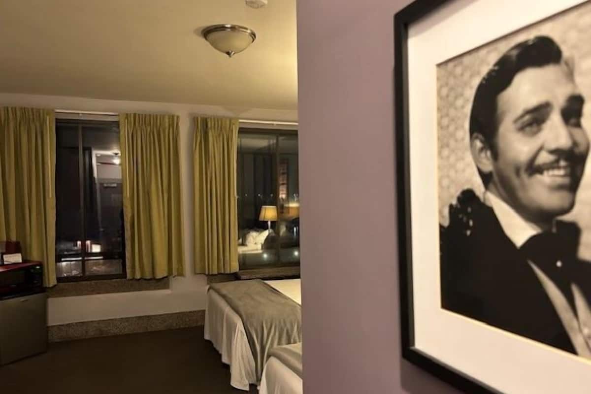 A hotel room with a bed, a desk, a chair, a lamp, and a window with curtains.