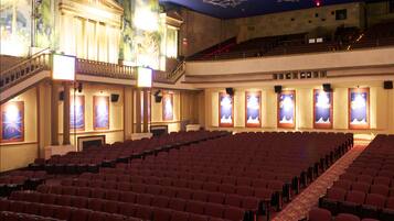 A theater with rows of red seats, a balcony, and a stage with a backdrop.