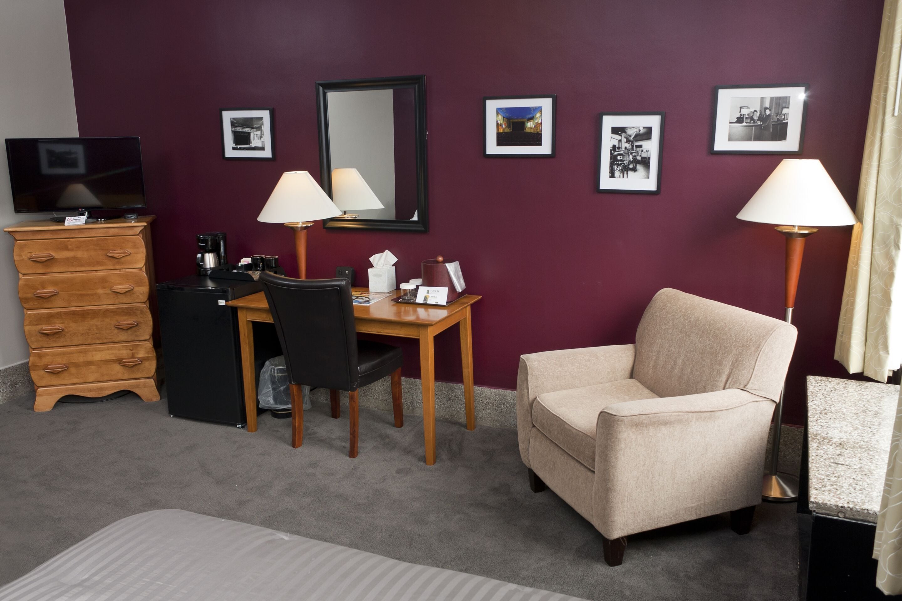 Une chambre d’hôtel comprenant un lit, un bureau avec une chaise, une commode, un téléviseur et des tableaux encadrés accrochés au mur.