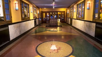 A hotel corridor with a central circular mosaic, flanked by doors and windows with light fixtures.
