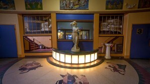 Un hall con una plataforma circular central, una estatua y una fuente. Hay pinturas en las paredes y una escalera a la izquierda.