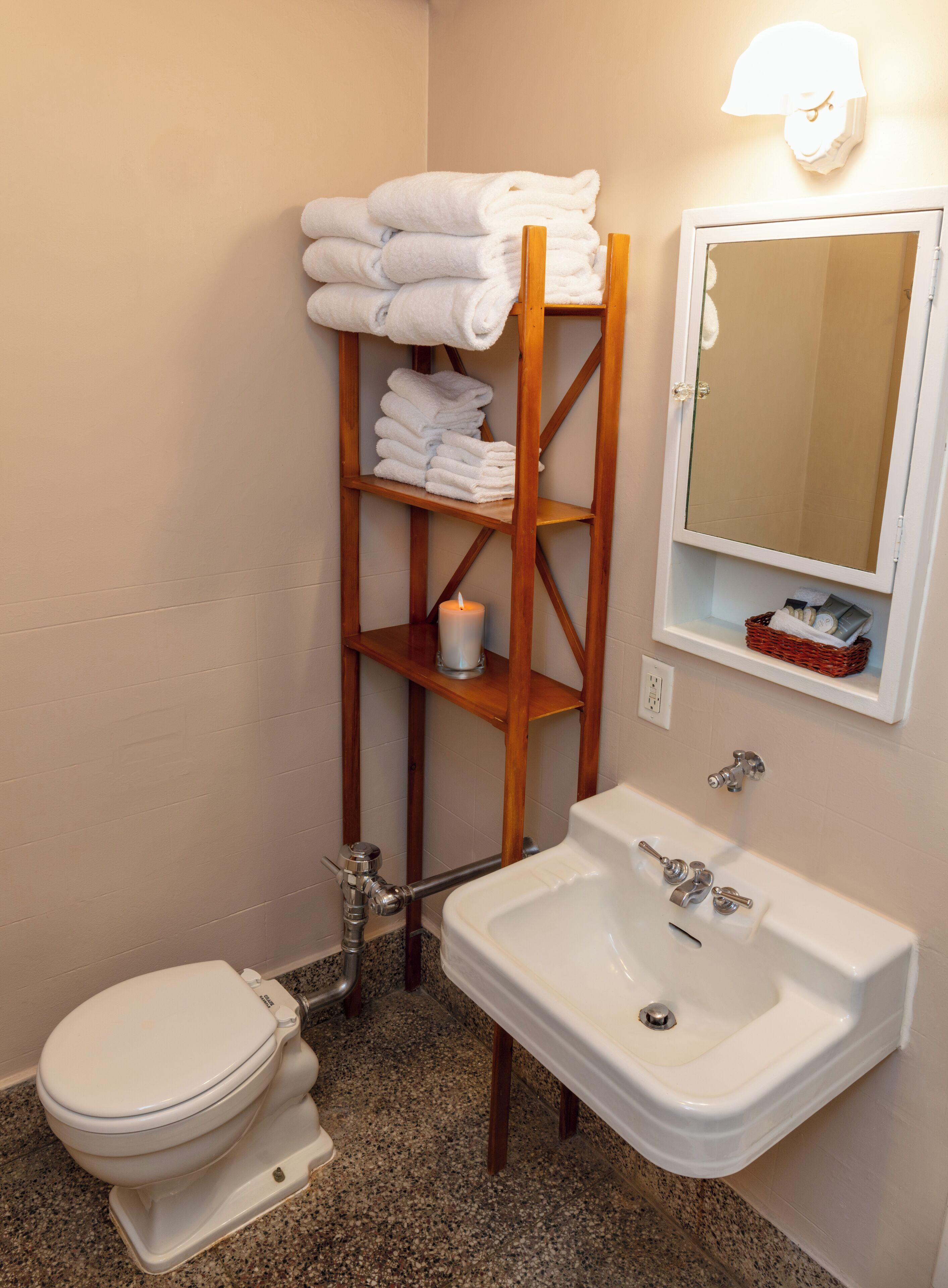 Un baño con inodoro, lavamanos y un estante de madera con toallas.