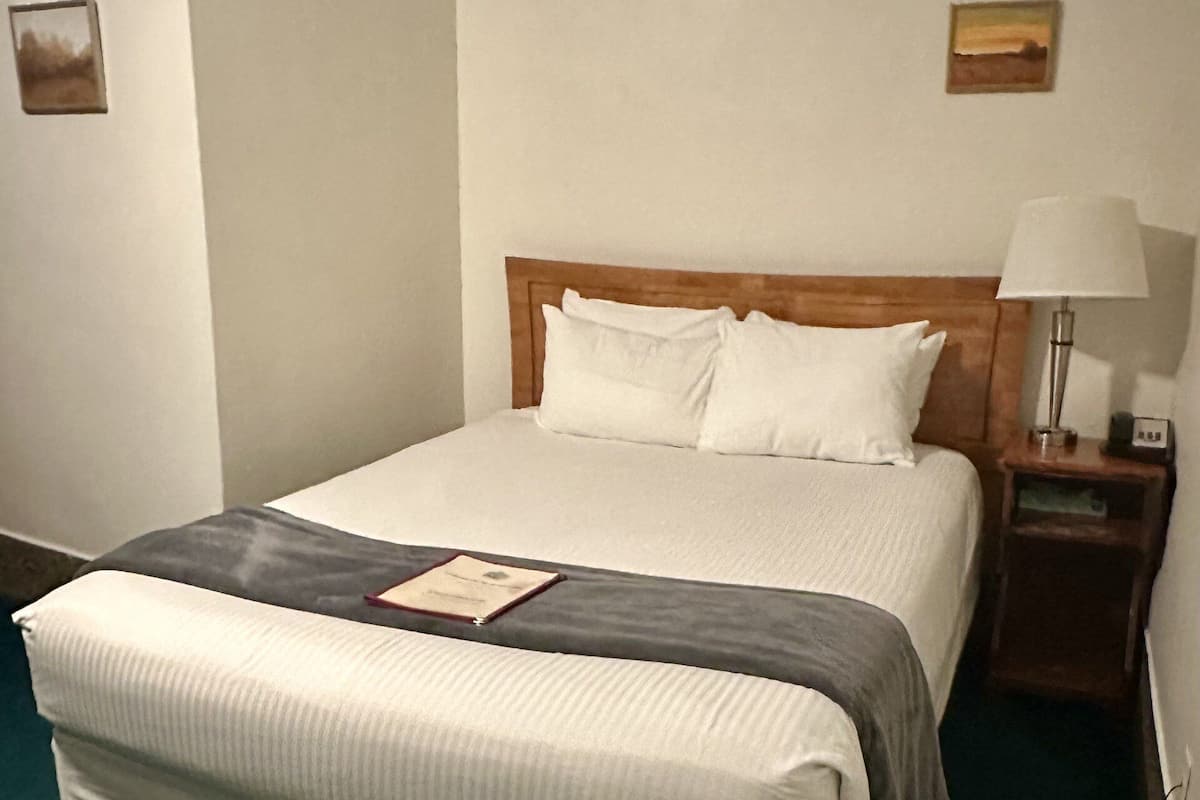 A neatly made bed with a wooden headboard, a bedside lamp, and a framed certificate on the nightstand.