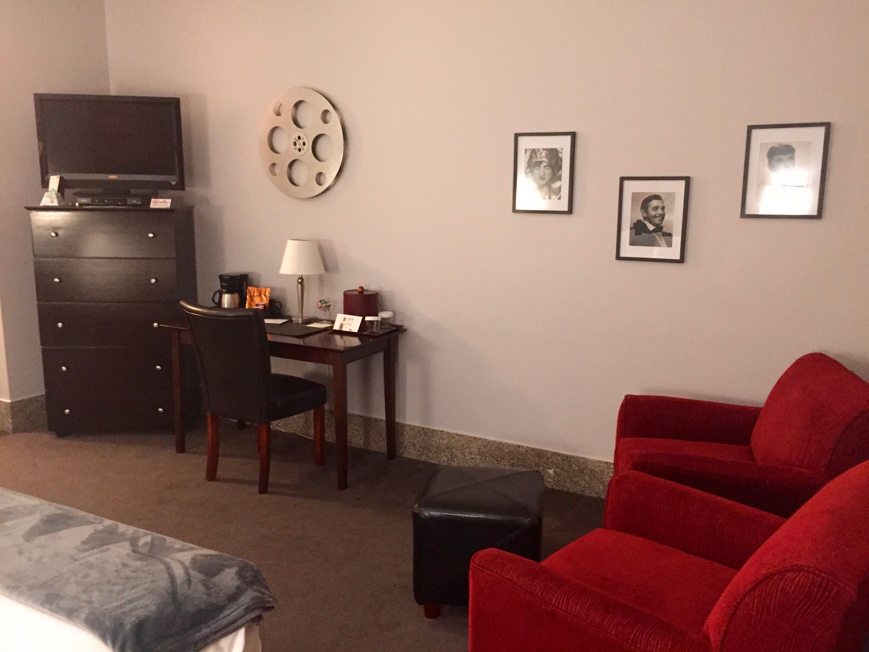 A hotel room with a bed, a desk with a chair, a television, a coffee machine, and a red sofa.