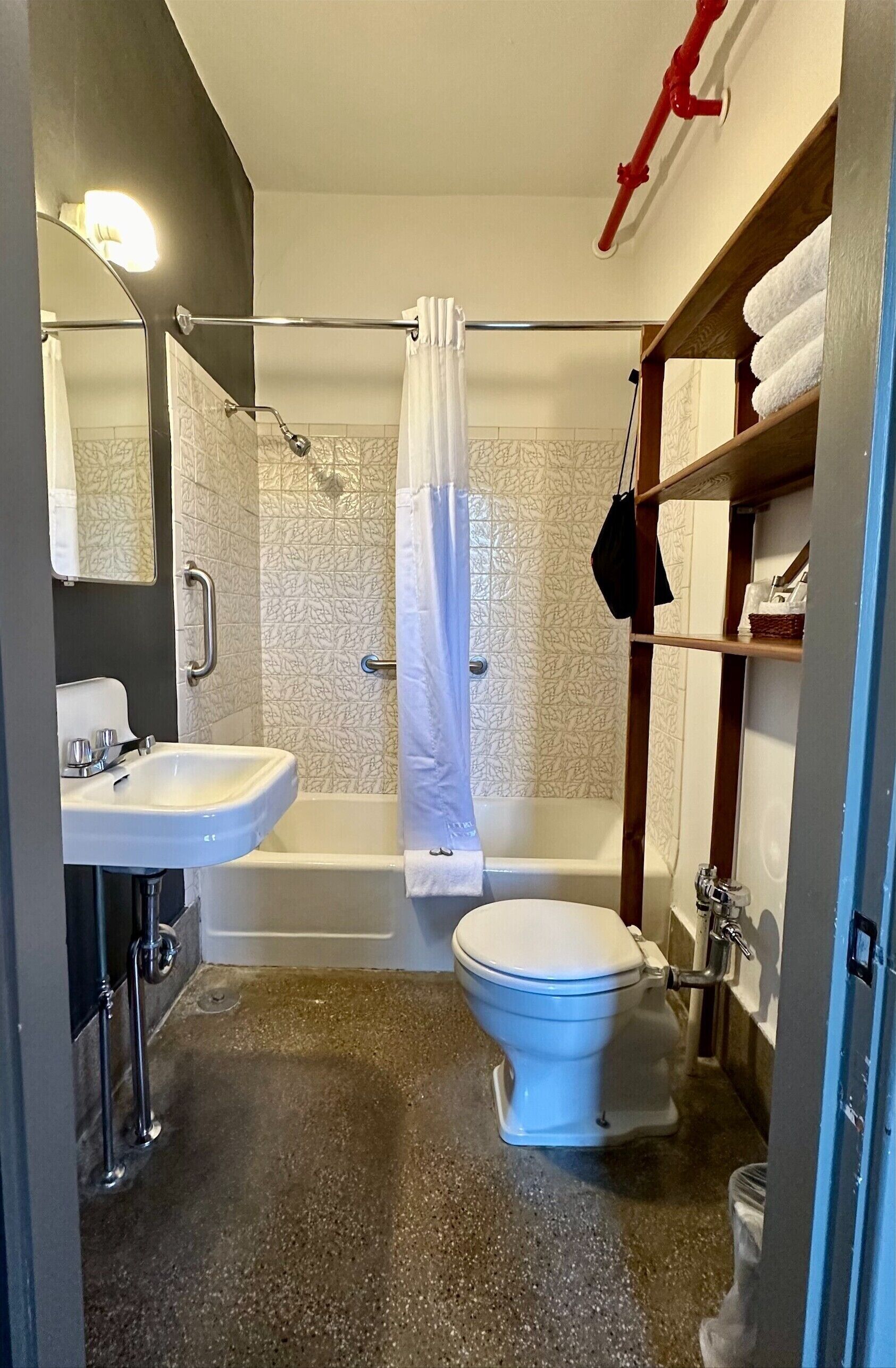 A bathroom with a white sink, toilet, and bathtub. There is a shower curtain, a towel rack, and a shelf with towels.