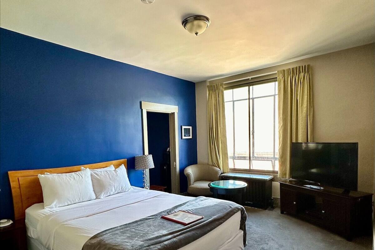 A hotel room with a large bed, a television, a chair, and a desk.