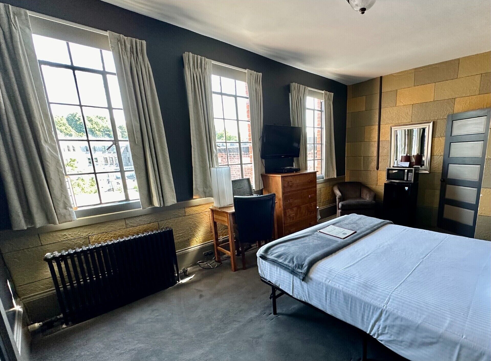 A hotel room with a bed, a desk, a chair, a TV, and a radiator.