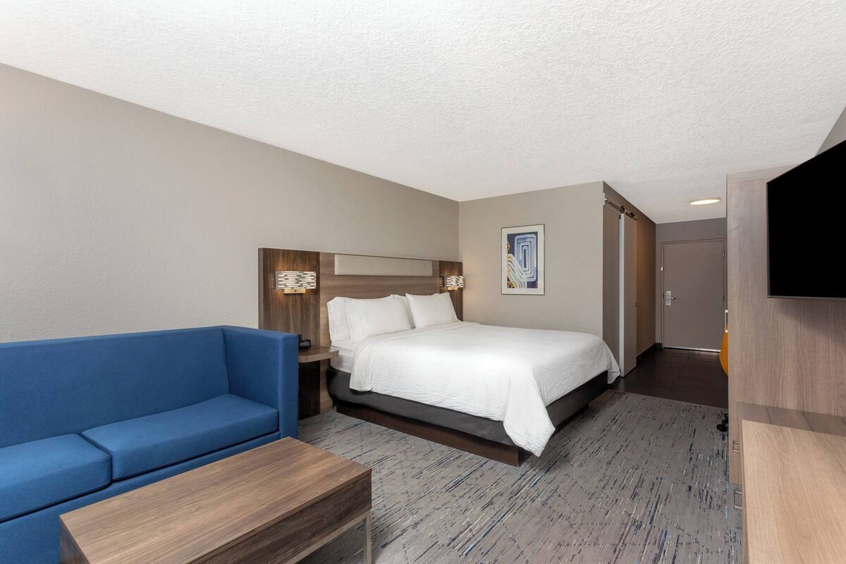 Une chambre d’hôtel avec un lit, un canapé bleu, une table de chevet en bois et un téléviseur à écran plat.