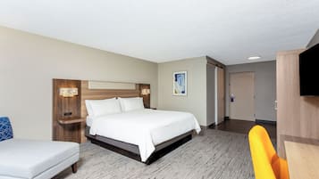 A hotel room with a bed, bedside tables, a chair, a TV, and a door.
