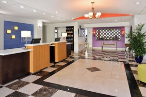 Zona de recepción de hotel con piso a cuadros, mostrador de recepción, área de descanso y una pared con un panel decorativo.