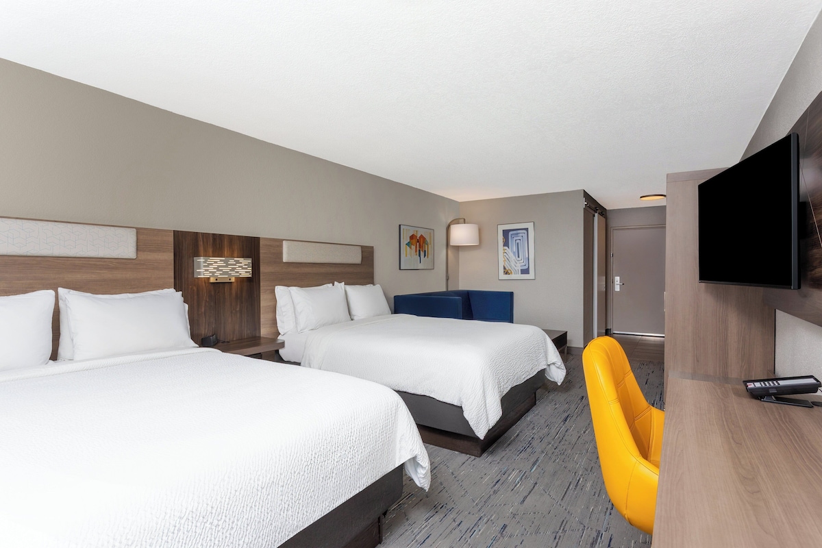 Quarto de hotel com duas camas, uma escrivaninha, uma cadeira e uma televisão.
