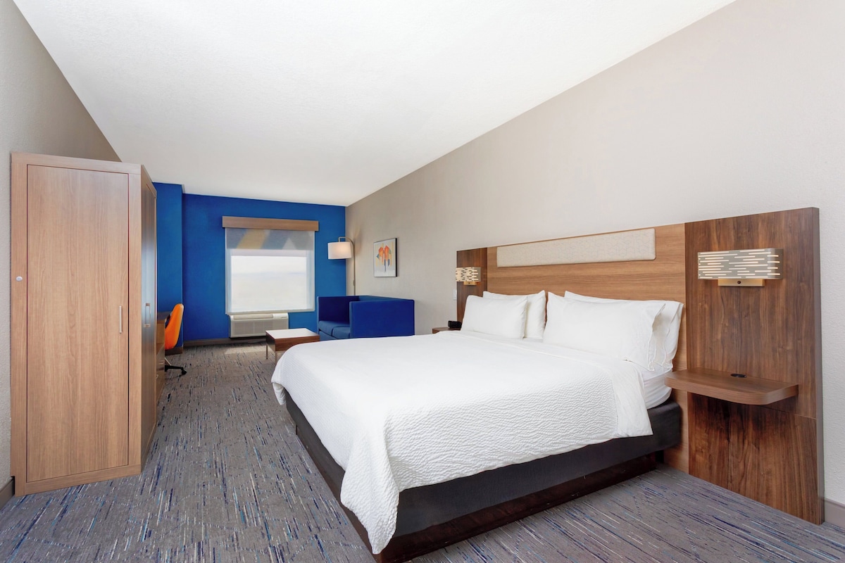 Quarto de hotel moderno com uma cama grande, uma escrivaninha, uma cadeira e um guarda-roupa.