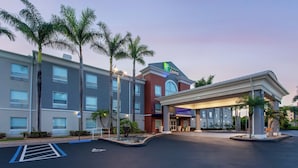 Un hotel Holiday Inn Express con un diseño moderno, que cuenta con un amplio estacionamiento, palmeras y una entrada bien iluminada.