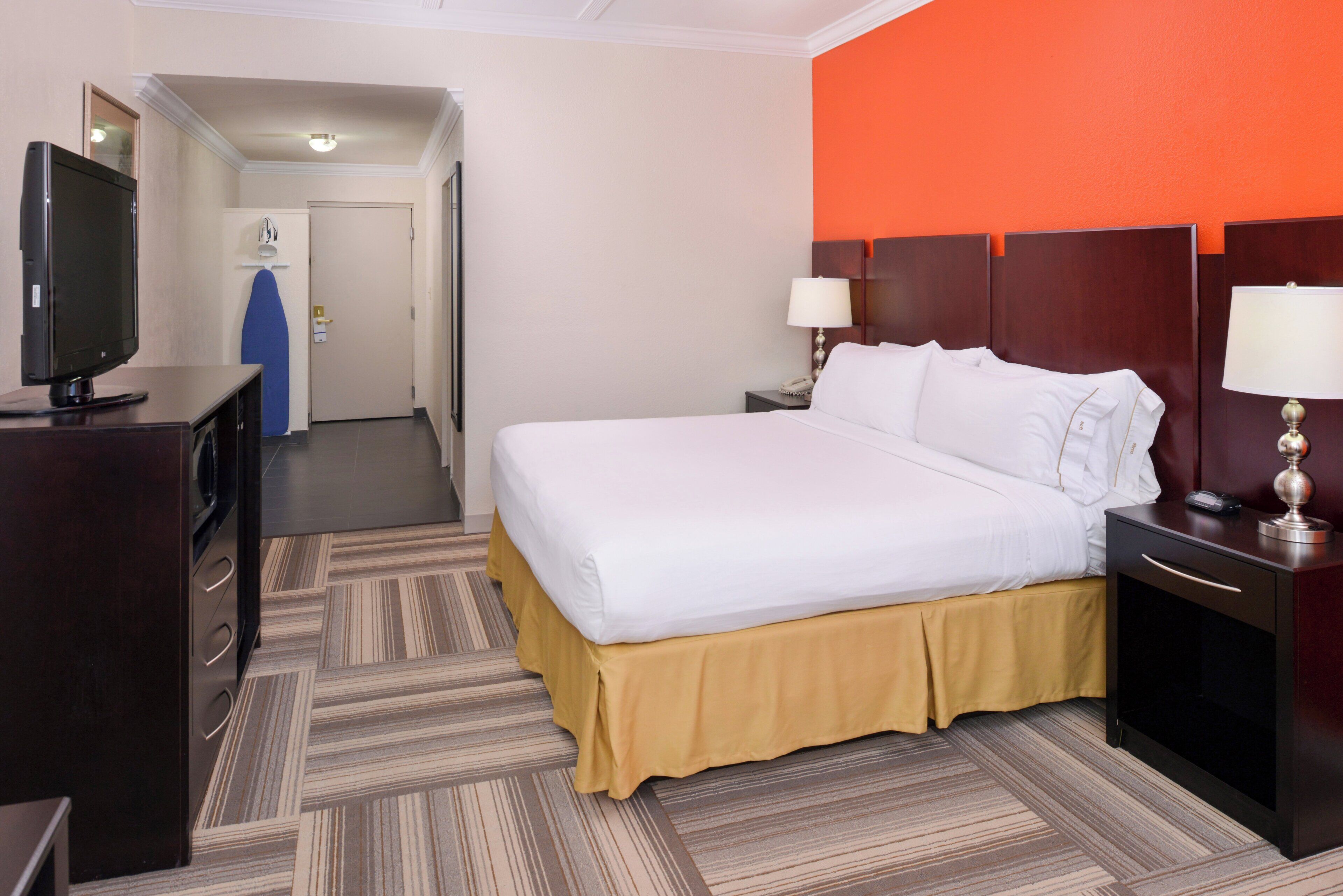 Een hotelkamer met een bed, nachtkastjes, een bureau, een televisie en een deur naar een gang.