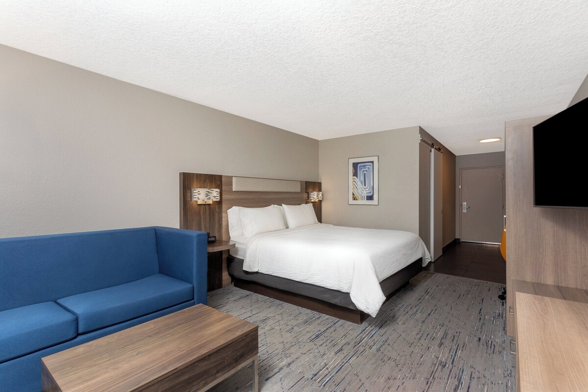 Ein Hotelzimmer mit Bett, blauem Sofa, Nachttisch aus Holz und Flachbildfernseher.