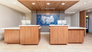Zona de recepción con dos mostradores de madera, un diseño geométrico azul y blanco en la pared, y un techo de madera con iluminación empotrada.