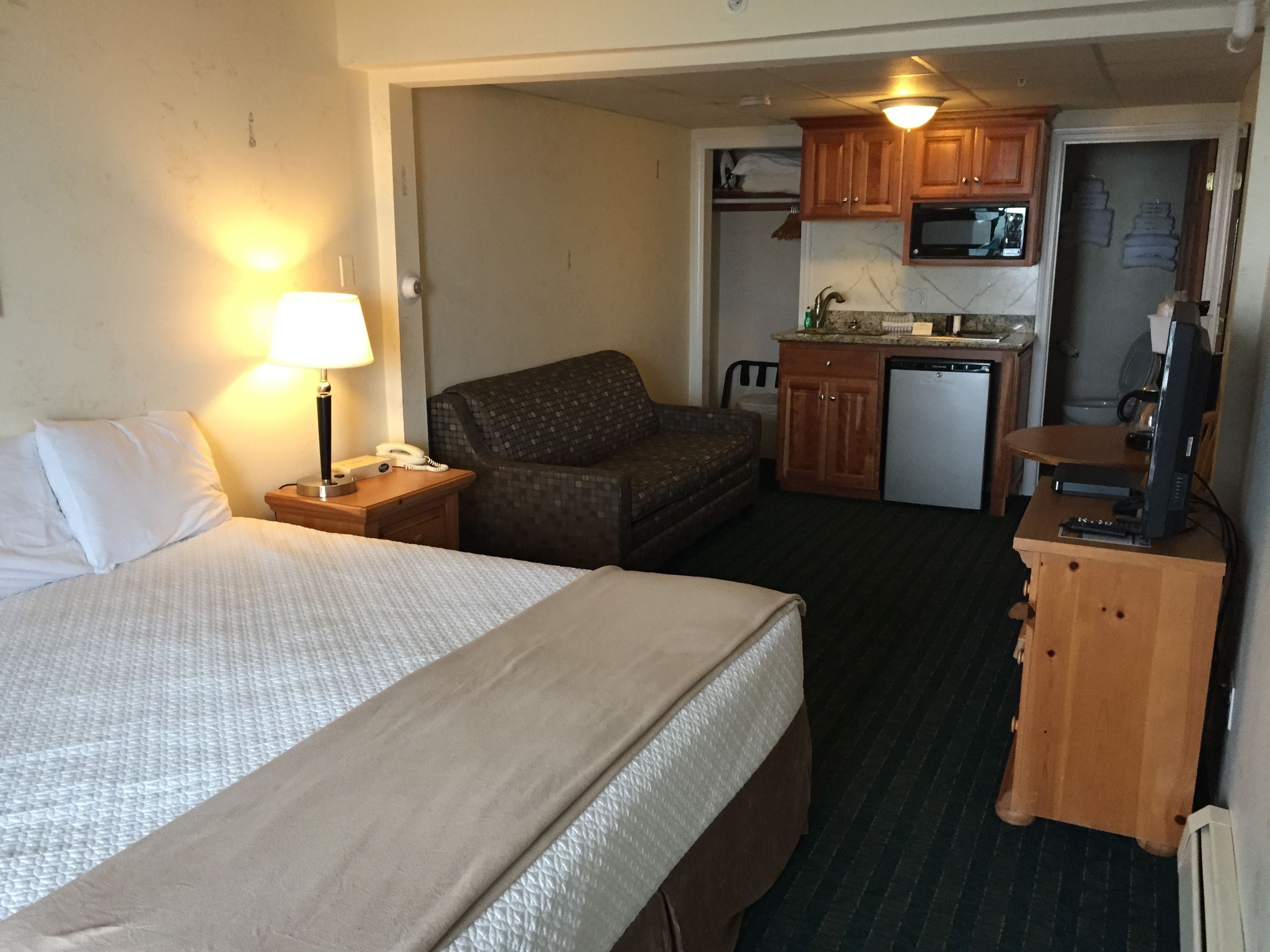 Habitación de hotel con cama, una silla, escritorio con computadora, microondas y pequeña kitchenette.