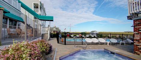 A pool area with lounge chairs, a hot tub, and a fenced deck with a view of the beach.