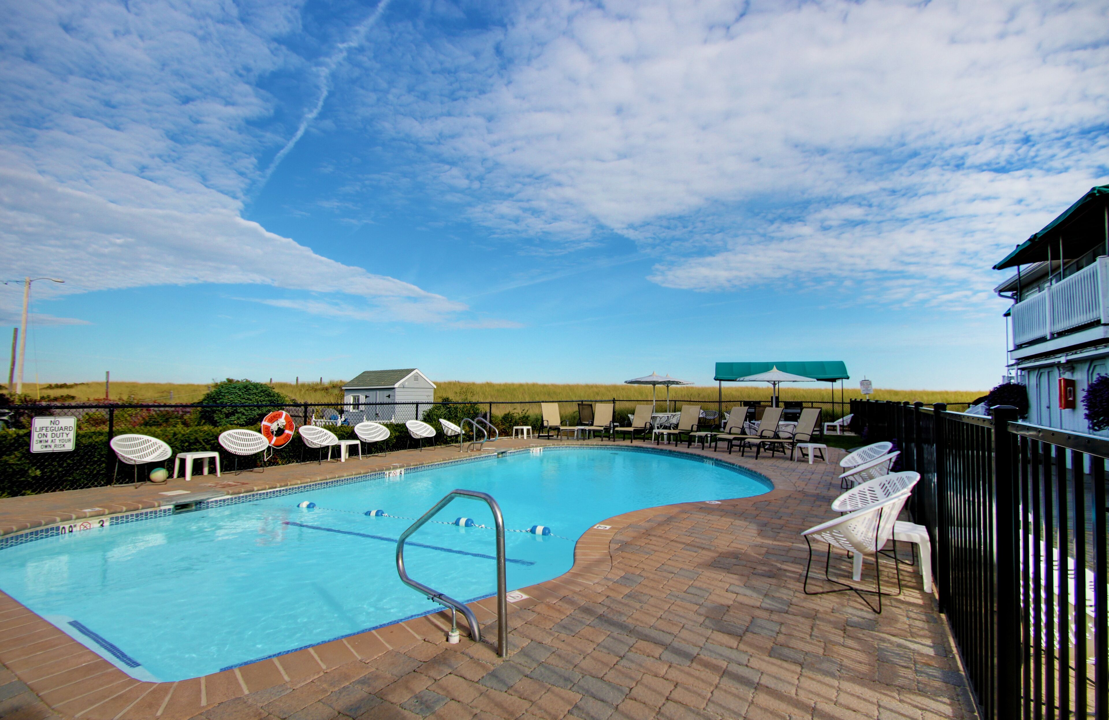 Une piscine entourée de chaises longues et de parasols, avec une terrasse en briques et une vue sur la campagne.