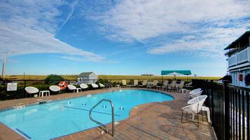 Une piscine entourée de chaises longues et de parasols, avec une terrasse en briques et une vue sur la campagne.