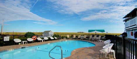 Une piscine entourée de chaises longues et de parasols, avec une terrasse en briques et une vue sur la campagne.
