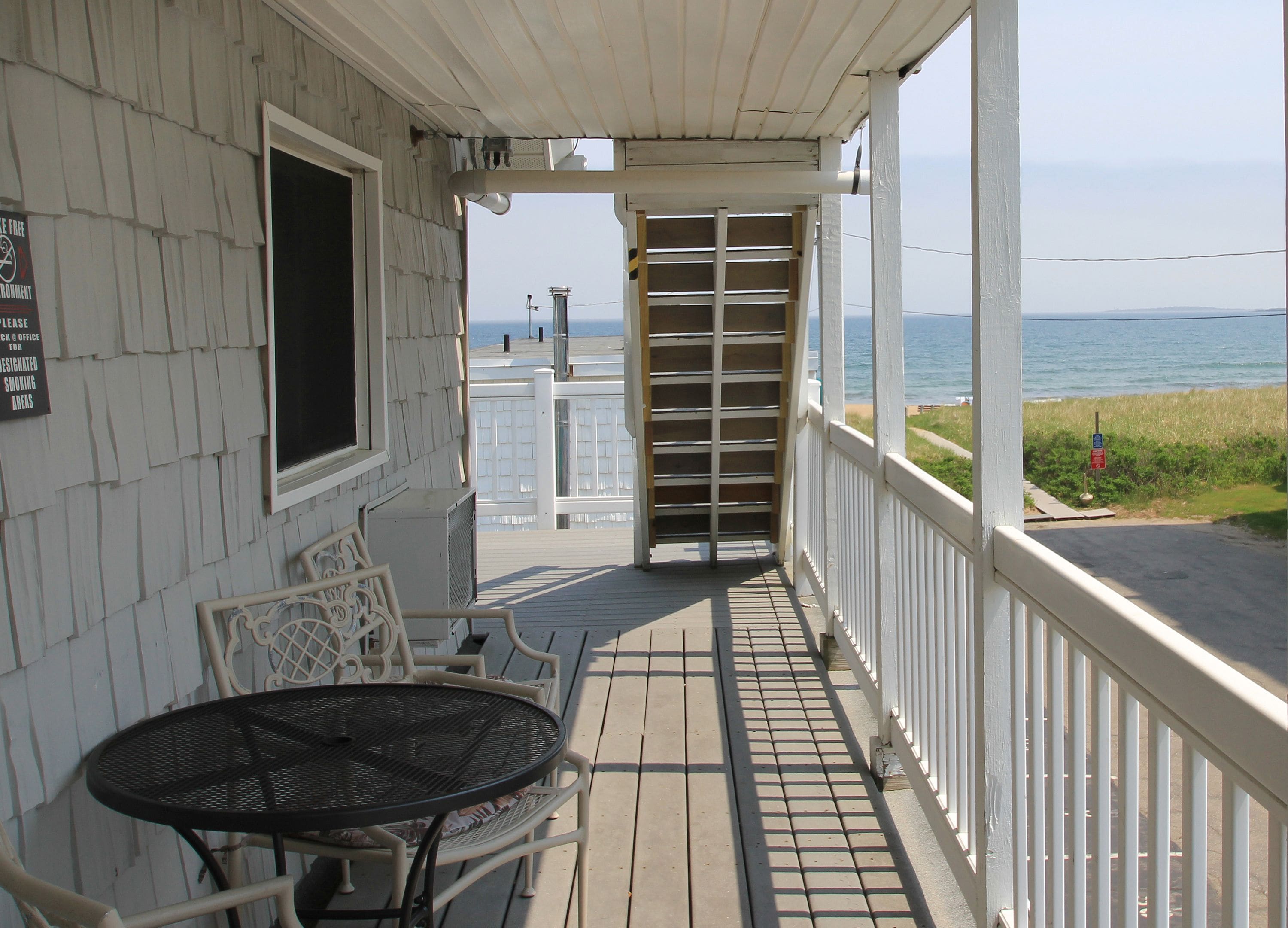 A covered porch with a table and chairs, a view of the ocean, and a sign indicating smoking is prohibited.