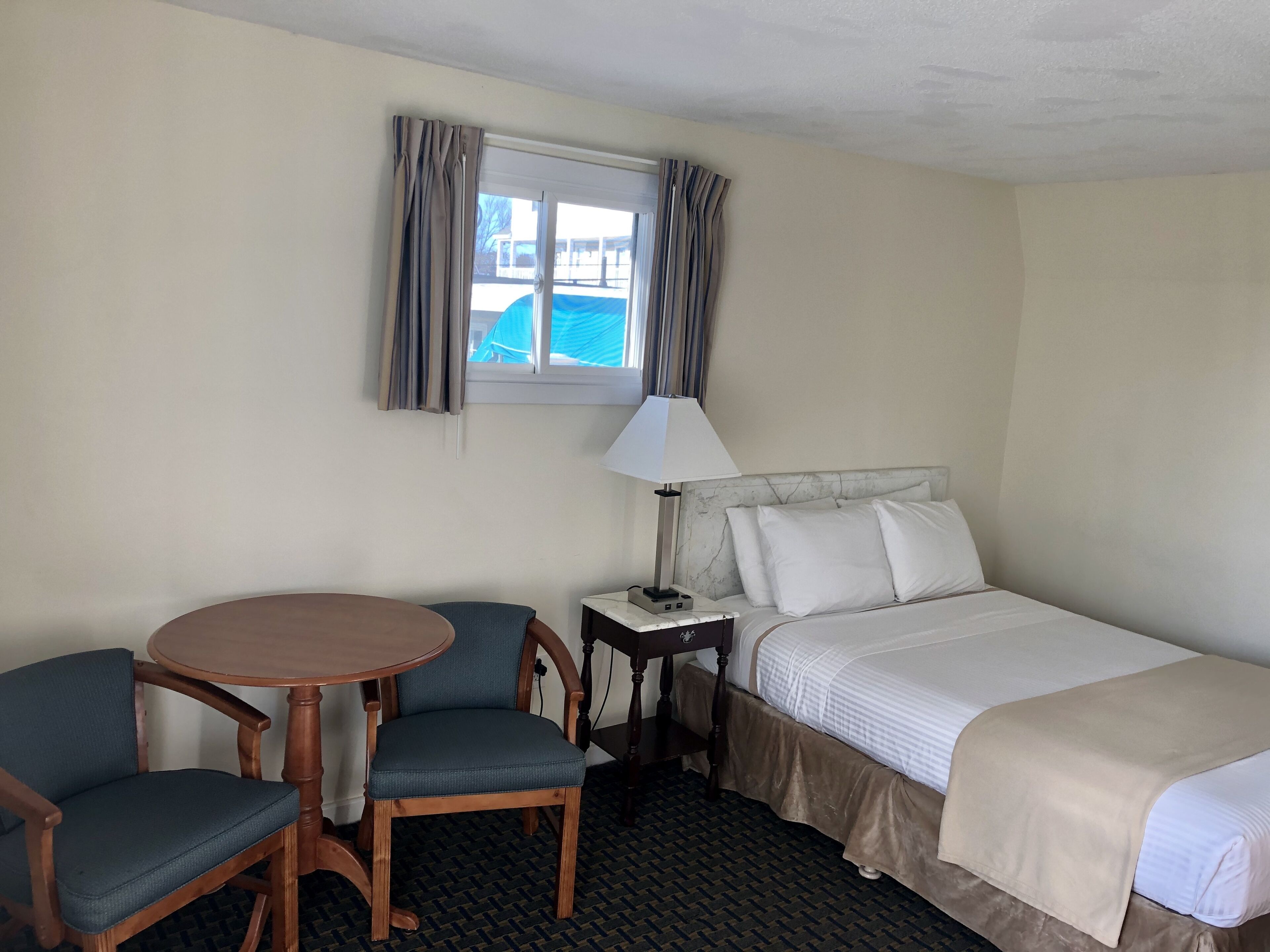 Een hotelkamer met een bed, een bureau met een lamp, een stoel en een raam met gordijnen.