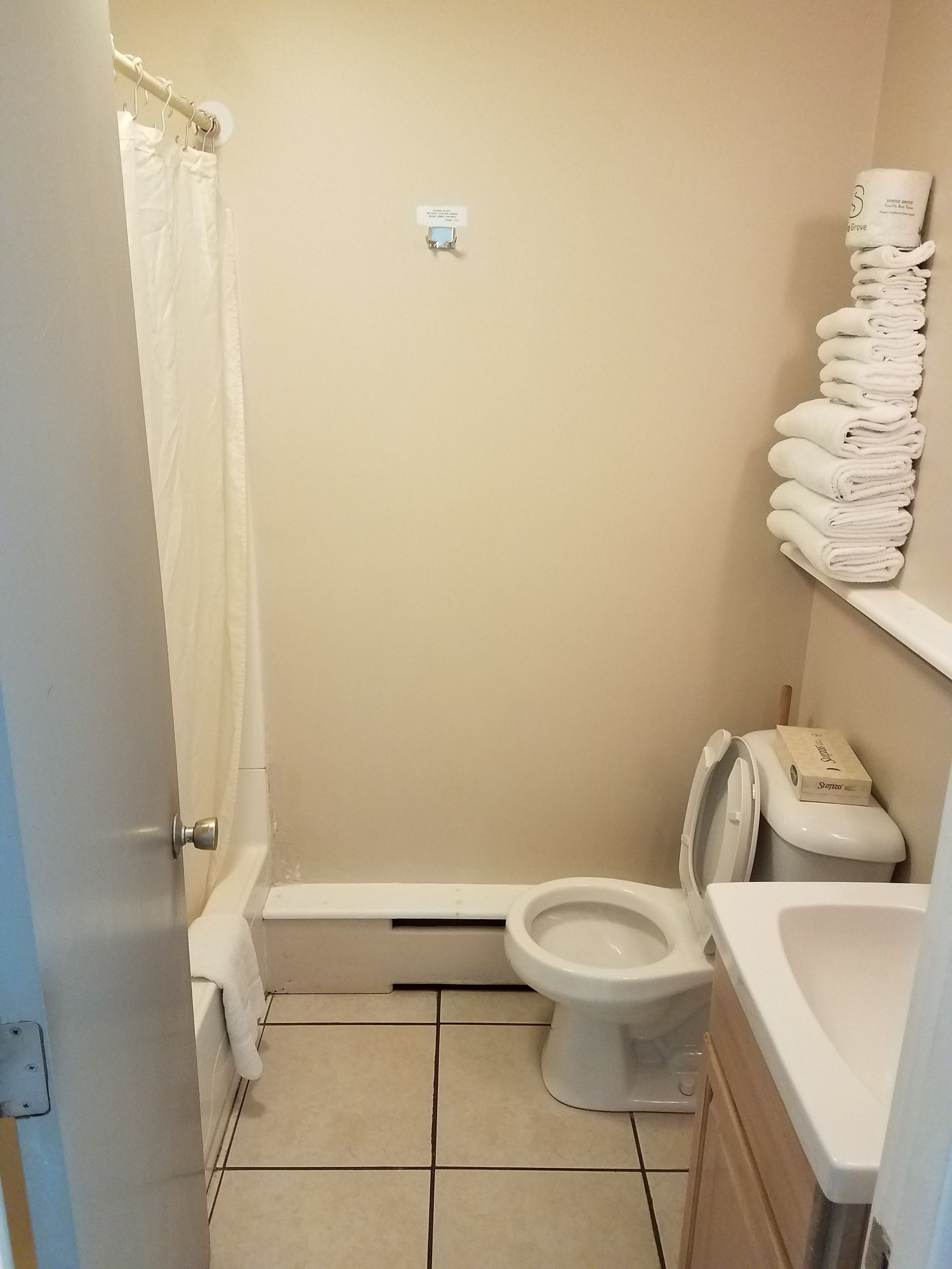 A small, clean bathroom with a toilet, a shower curtain, and a stack of towels on a shelf.