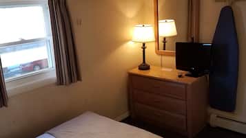 A hotel room with a bed, a nightstand with a lamp, a television, and an ironing board.