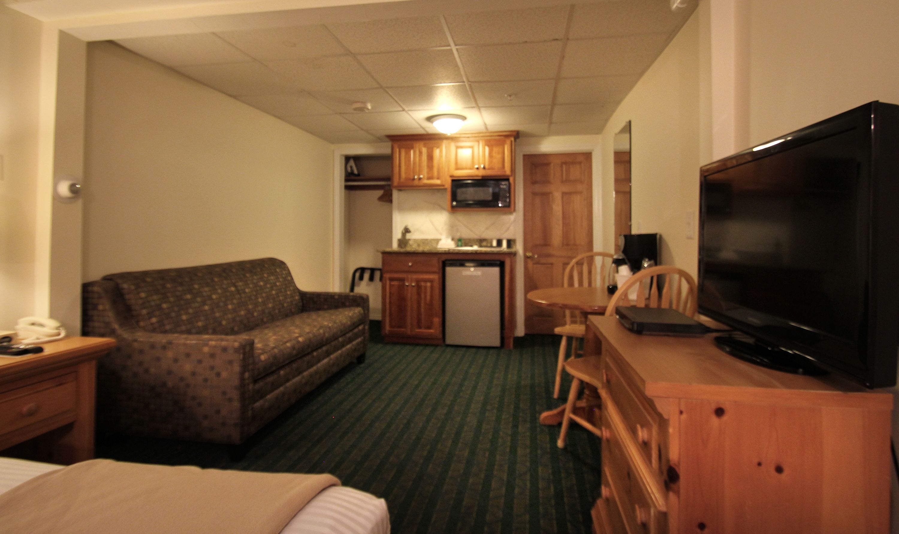 A compact hotel room with a sofa, a small kitchenette, a television, and a dining table.