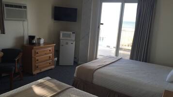 Quarto de hotel com duas camas, televisão, micro-ondas, cafeteira, cómoda e vista para a praia.