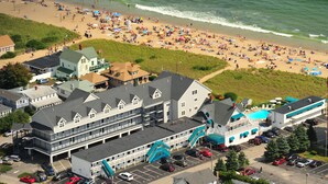 Un hotel frente al mar, con varios pisos, estacionamiento y una playa al fondo.