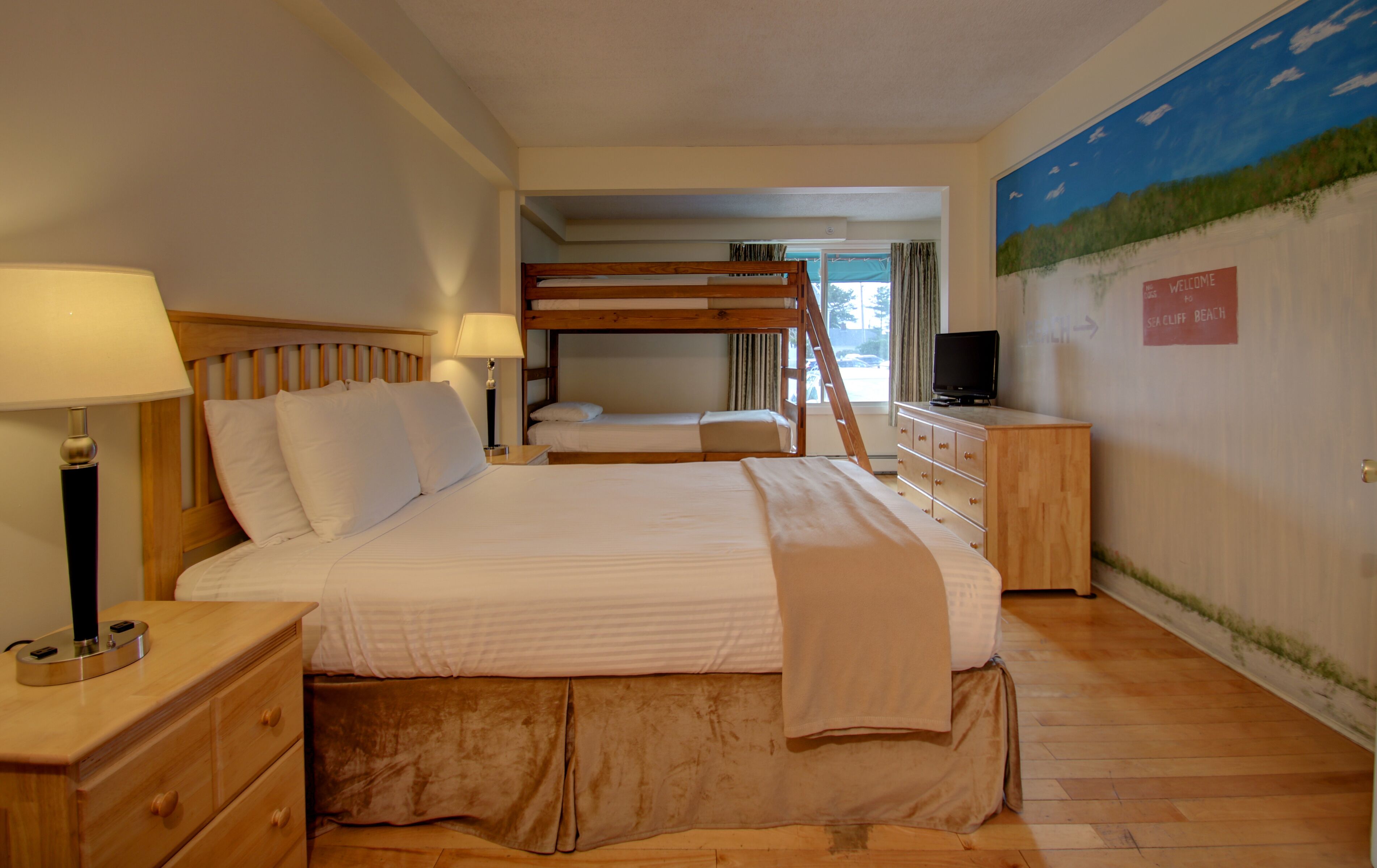 Una habitación de hotel con una cama grande, una cama nido, un televisor y un cuadro en la pared.