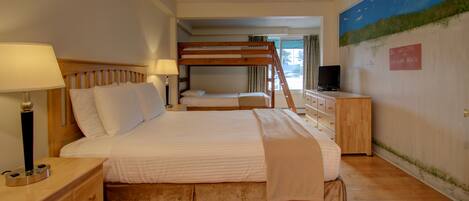 Una habitación de hotel con una cama grande, una cama nido, un televisor y un cuadro en la pared.