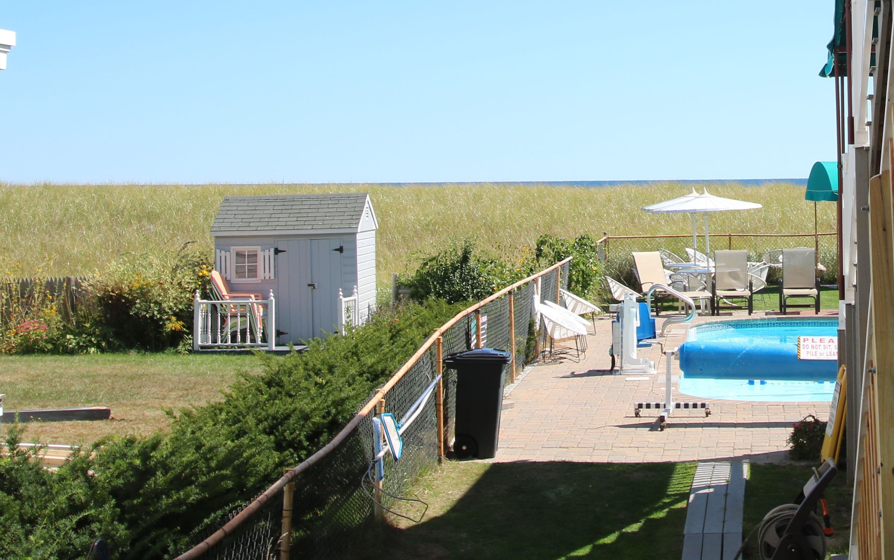 A pool area with a small shed, a fenced deck, and lounge chairs.