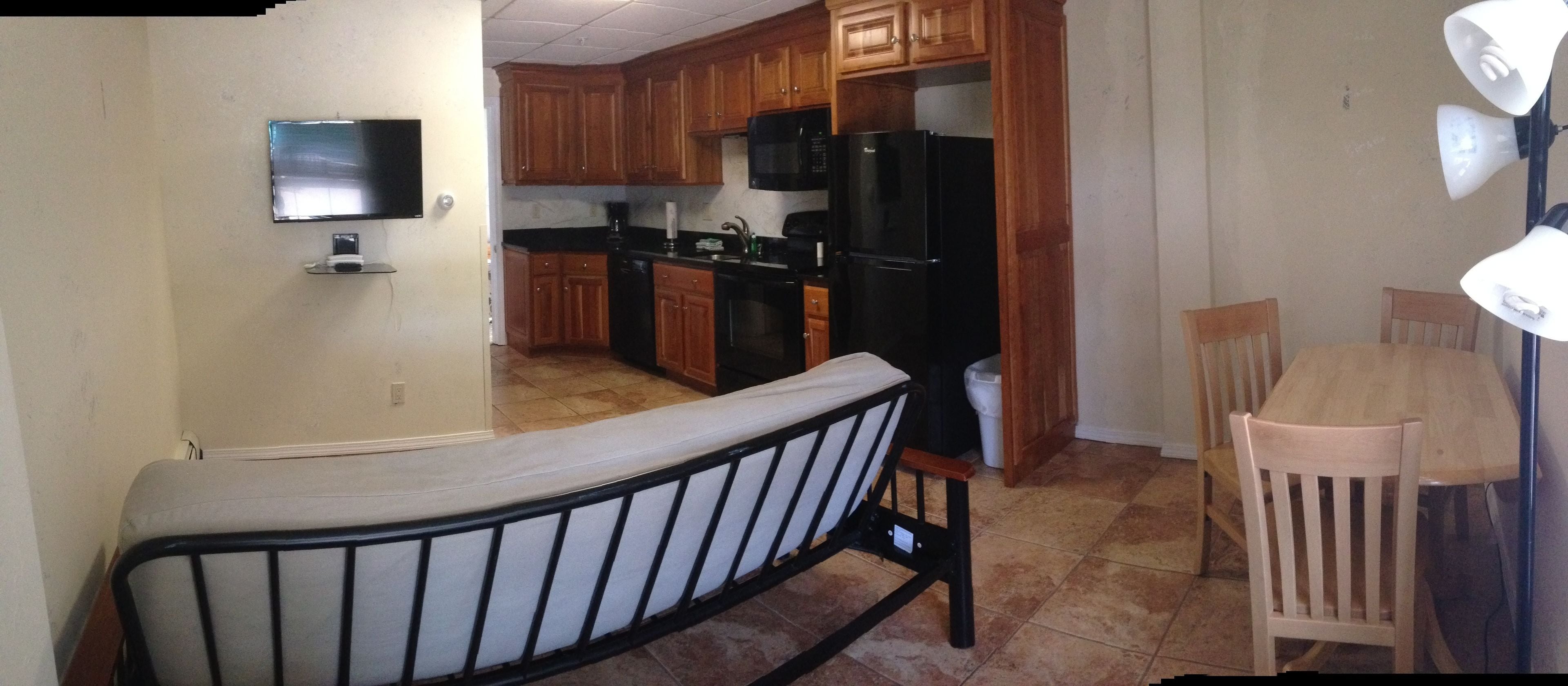 A compact kitchen with wooden cabinets, a black refrigerator, and a dining area with a wooden table and chairs.