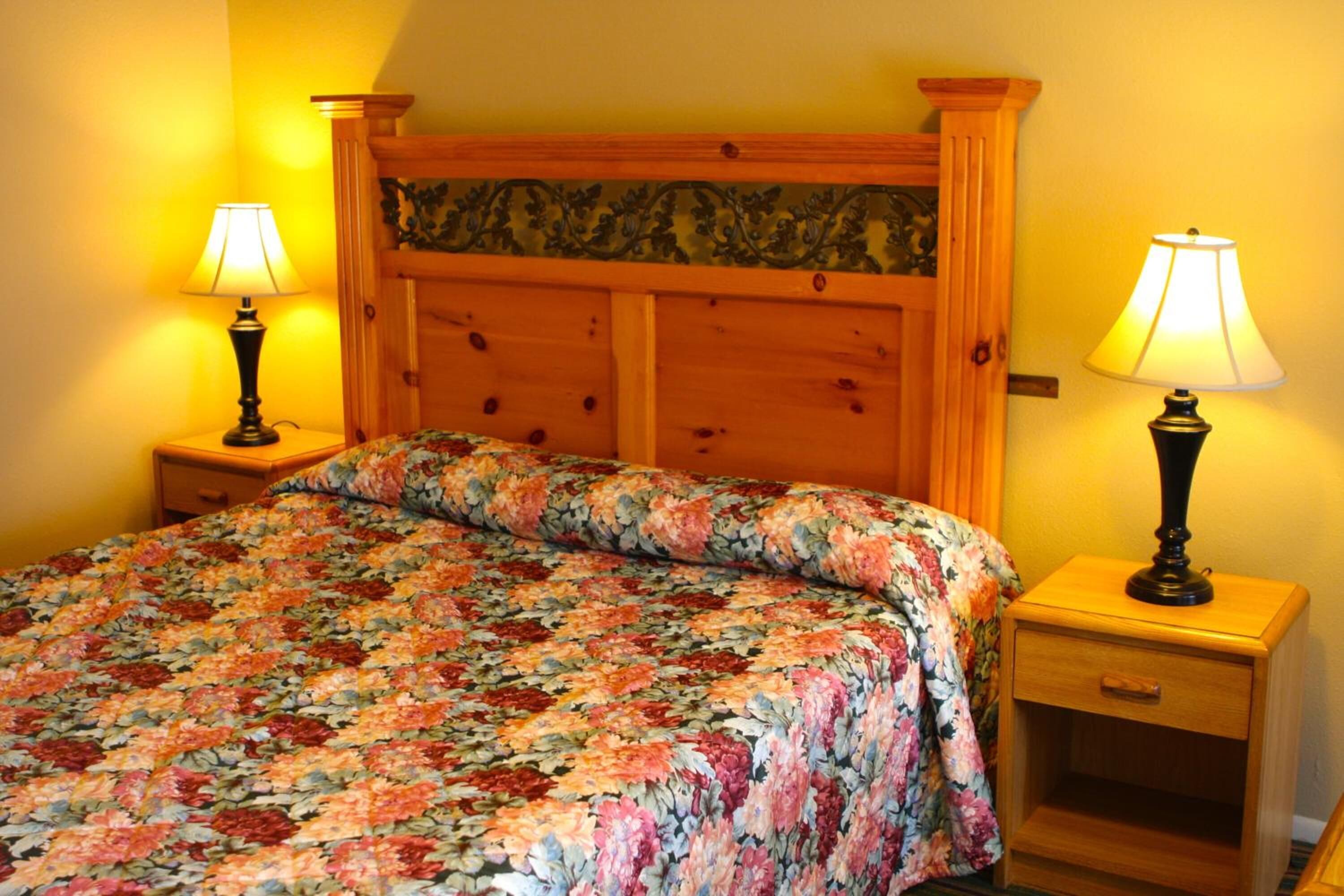 Un letto con copriletto floreale, una testiera in legno, due comodini con lampade e un tavolino notte con cassetto.